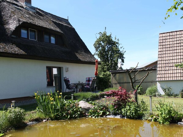 A thatched-roof house with a garden and a pond. - Ferienwohnung in Pepelow in Strandnahe (Am Salzhaff)