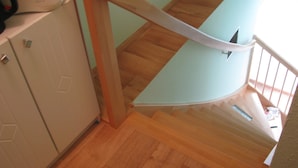 Una escalera de madera con barandilla de vidrio que lleva a un rellano con un tostador y armarios.