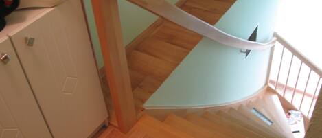 A wooden staircase with a glass handrail, leading to a landing with a toaster and cabinets.