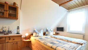 Un dormitorio acogedor con una cama nido de madera, una mesita de noche con lámpara, un aparador y una ventana con cortinas.