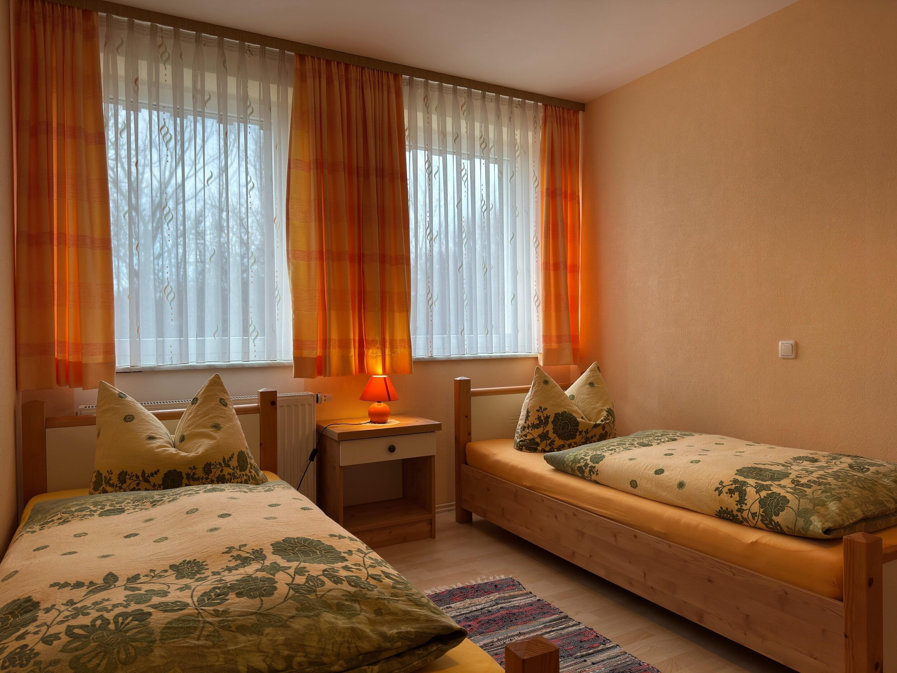 A bedroom with two beds, a nightstand, a lamp, and a window with curtains.