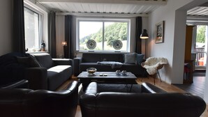 A modern living room with a dark sofa set, a coffee table, and a large window with decorative glass panels. - Chalet in Levinska Ole Near Giant Mountains (Levínská Olešnice)