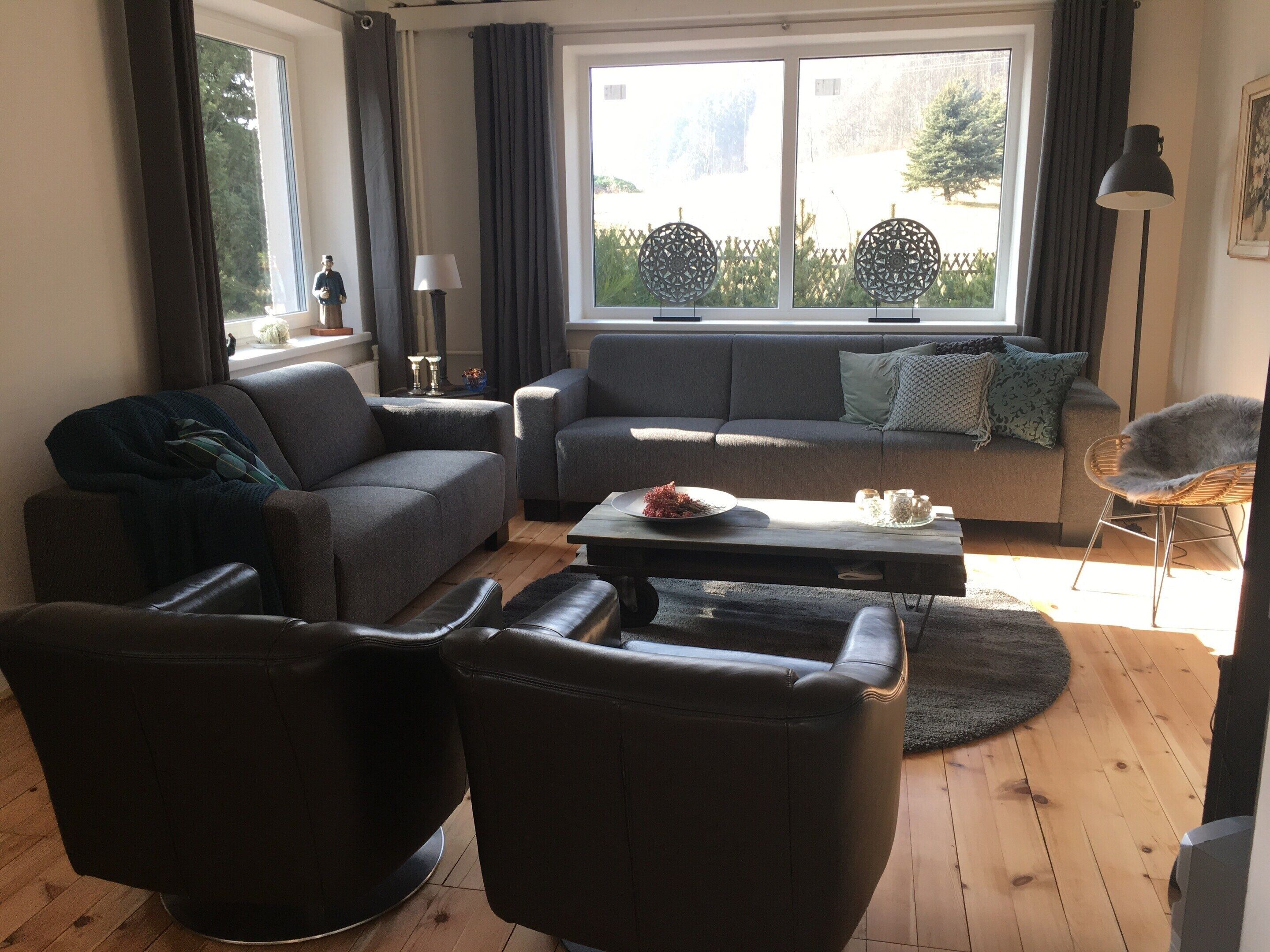 Una sala de estar con un sofá, dos sillones, una mesita de centro y una ventana con cortinas.