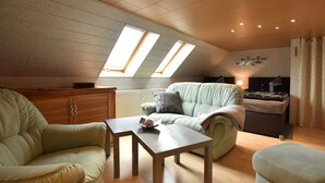 A cozy loft bedroom with a sloped ceiling, wooden flooring, a green sofa, a small table, and a bed with a headboard. - Moderne Ferienwohnung mit Grill in Rakow (Am Salzhaff)