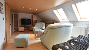 A cozy attic bedroom with a sloped ceiling, a large window, a television, a comfortable chair, and a bed. - Moderne Ferienwohnung mit Grill in Rakow (Am Salzhaff)