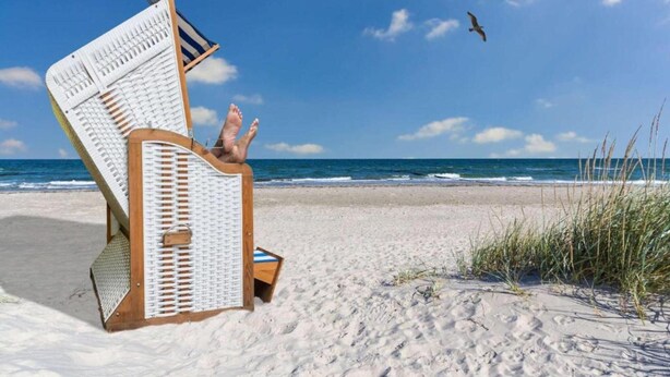 A beach chair with a person reclining, overlooking a sandy beach and ocean. - Moderne Ferienwohnung mit Grill in Rakow (Am Salzhaff)