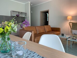 A modern living room with a brown leather sofa, a white armchair, a glass coffee table, and a dining table with a vase of flowers. - Grosszuegige Ferienwohnung mit Garten (Saal)