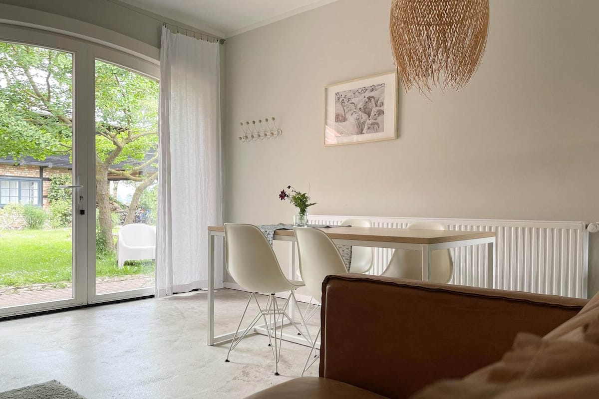 Ein modernes Schlafzimmer mit großem Fenster, einem Essbereich mit Stühlen, einem Tisch und einer Pendelleuchte.