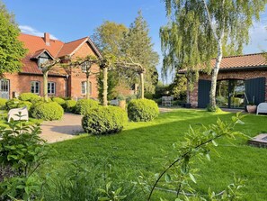 A brick house with a red-tiled roof, surrounded by well-maintained hedges and a grassy lawn. - Grosszuegige Ferienwohnung mit Garten (Saal)