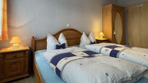 A bedroom with two beds, wooden headboards, bedside lamps, and a wardrobe. - Charmante Ferienwohnung mit Garten in Wiek (Wiek)