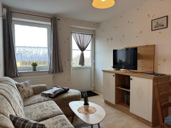 Un salon chaleureux avec un canapé, une petite table, un téléviseur posé sur un meuble en bois et une fenêtre avec des rideaux.