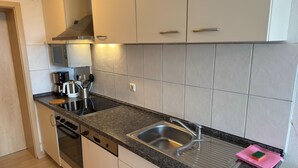 A modern kitchen with white cabinets, a stainless steel sink, a coffee maker, and a dishwasher. - Charmante Ferienwohnung mit Garten in Wiek (Wiek)