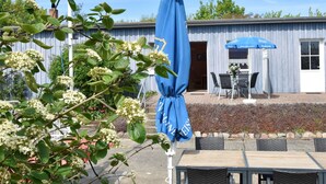An outdoor seating area with a table and chairs, a blue umbrella, and a building with a wooden facade. - Charmante Ferienwohnung mit Garten in Wiek (Wiek)