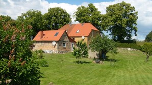 Ein Haus aus Stein mit rotem Dach, umgeben von einem gepflegten Rasen und Bäumen.