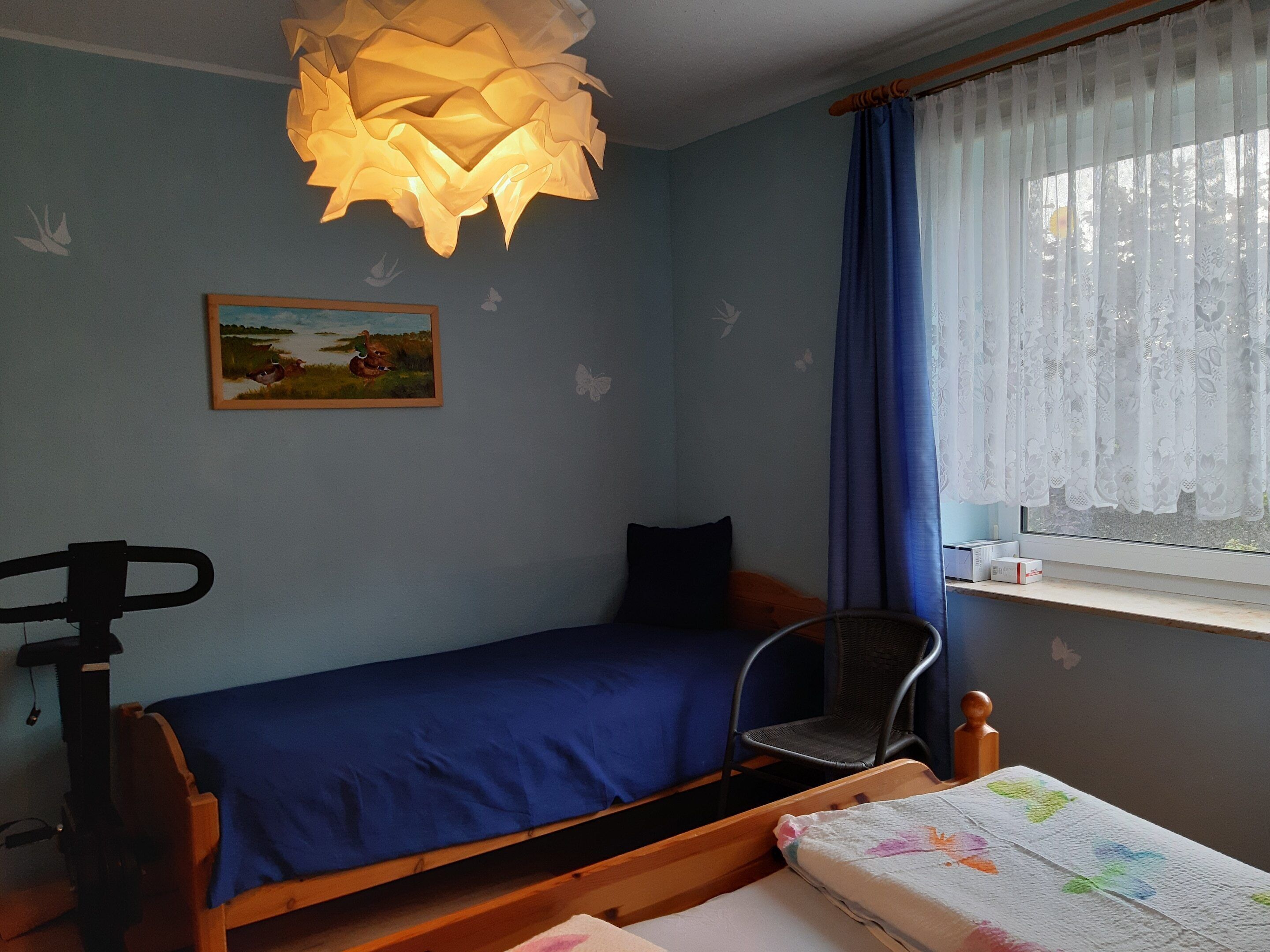 A small, cozy room with a single bed, a chair, a desk, and a window with curtains.