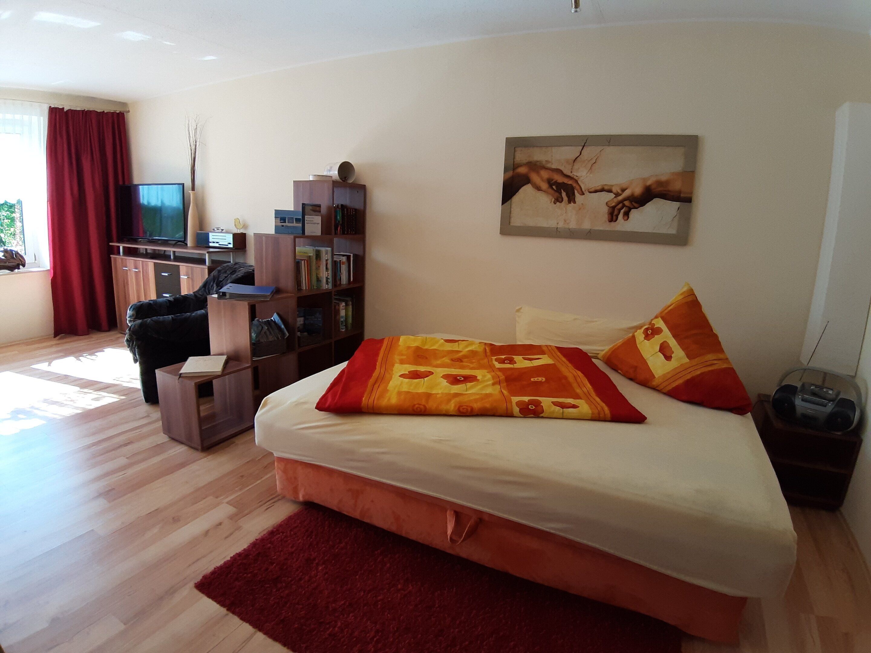 A bedroom with a bed, a desk, a bookshelf, and a painting on the wall.