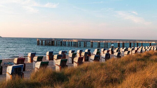 Ein Strand mit Liegestuhlreihen und einem Steg, der ins Wasser führt.