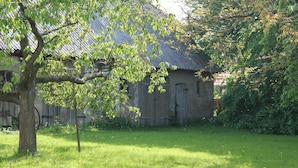 A rustic building with a sloped roof, surrounded by a grassy area with a tree in the foreground.