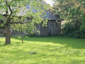 A rustic building with a sloped roof, surrounded by a grassy area with a tree in the foreground.