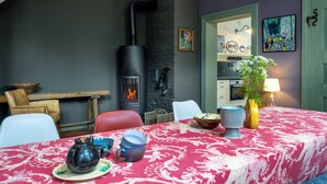 Een gezellige kamer met een open haard, een eettafel gedekt met een rode tafelkleed en diverse serviesdelen.