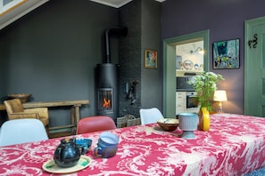 Une pièce chaleureuse avec une cheminée, une table à manger dressée avec une nappe rouge et une variété d’articles de vaisselle.