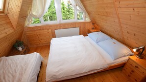 Dormitorio de una cabaña de madera con cama, mesita de noche y ventana con cortinas.