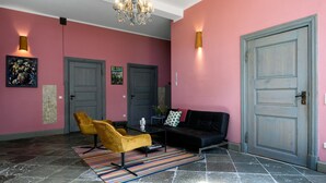 A hallway with a pink wall, a black sofa, a yellow chair, a chandelier, and two doors. - Steffenshagen Vicarage Retreat (Steffenshagen)