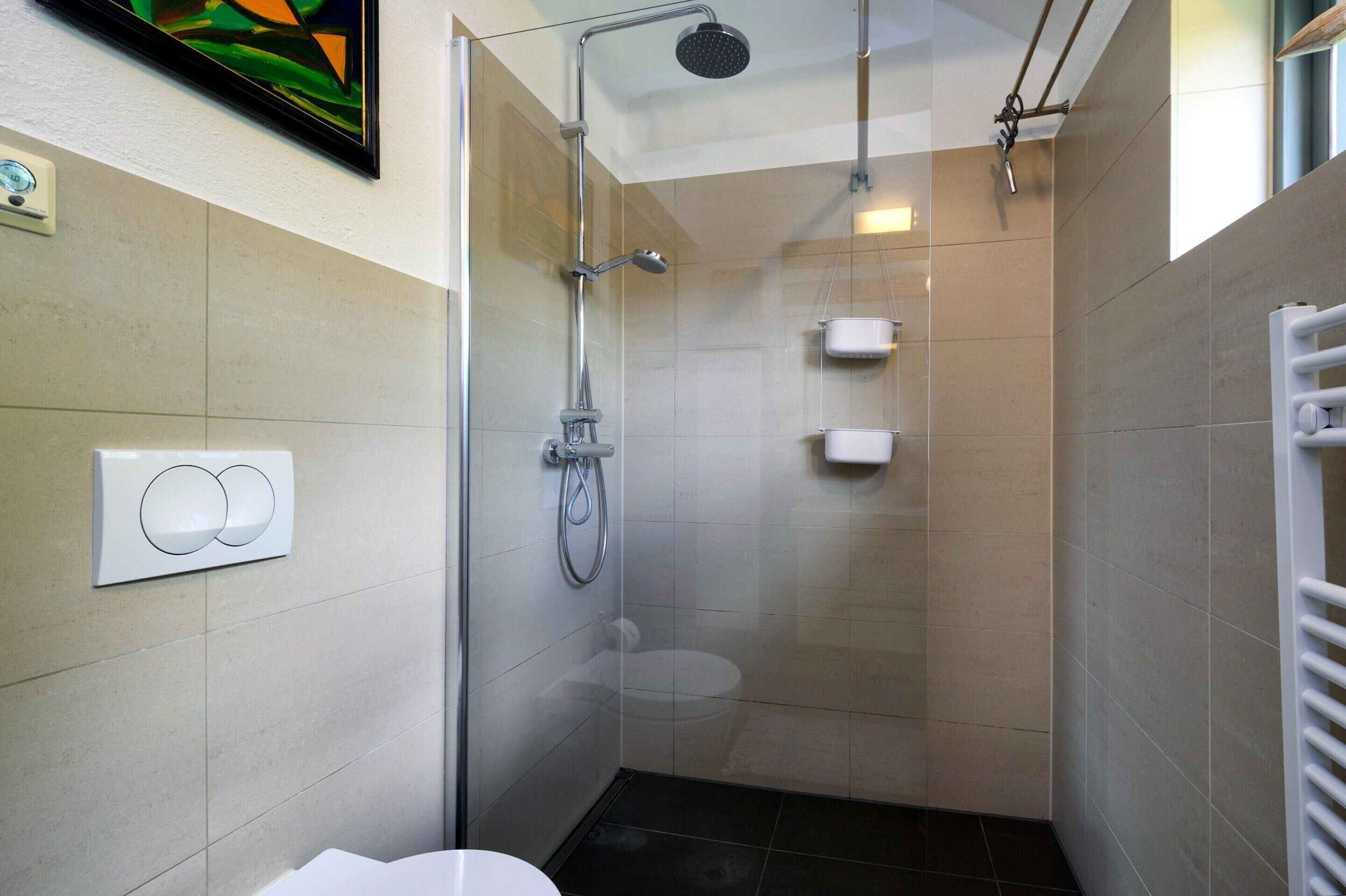 A modern bathroom with a glass-enclosed shower, a toilet, and a towel rack.
