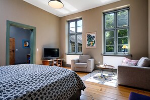 A room with a bed, a television, a sofa, and a chair. There are large windows and a door. - Steffenshagen Vicarage Retreat (Steffenshagen)