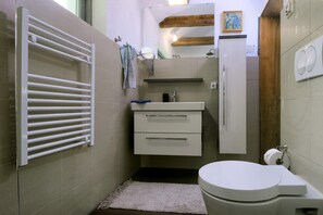 Un baño pequeño con inodoro blanco, lavamanos con espejo arriba y toallero con dos toallas.