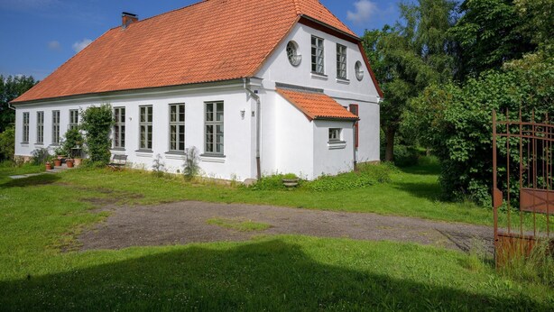 A two-story white house with a red-tiled roof, surrounded by greenery and a gravel path. - Steffenshagen Vicarage Retreat (Steffenshagen)