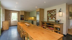 Cucina spaziosa con un lungo tavolo in legno e sedie, dotata di elettrodomestici moderni e una colonna a parete.