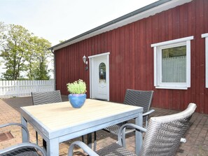 An outdoor patio with a table and chairs, a potted plant, and a red building with a white door and window. - Sunny Apartment in Wiek, Rugen (Wiek)