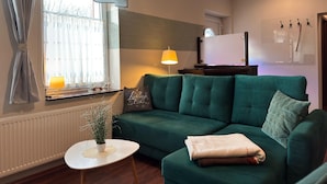 A living room with a green sofa, a small round table with a plant, a lamp, and a window with curtains. - Sunny Apartment in Wiek, Rugen (Wiek)