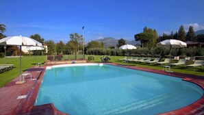 Ein Swimmingpool mit roter Ziegelumrandung, umgeben von weißen Sonnenschirmen und Liegestühlen.
