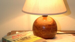 Eine Tischlampe mit Holzfuß und weißem Lampenschirm, platziert auf einem Tisch neben einem Buch mit dem Titel „Belle Toscane“ von Frances Mayes.