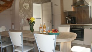 Een moderne keuken met een houten eettafel, witte stoelen, een vaas met bloemen en een fruitschaal.