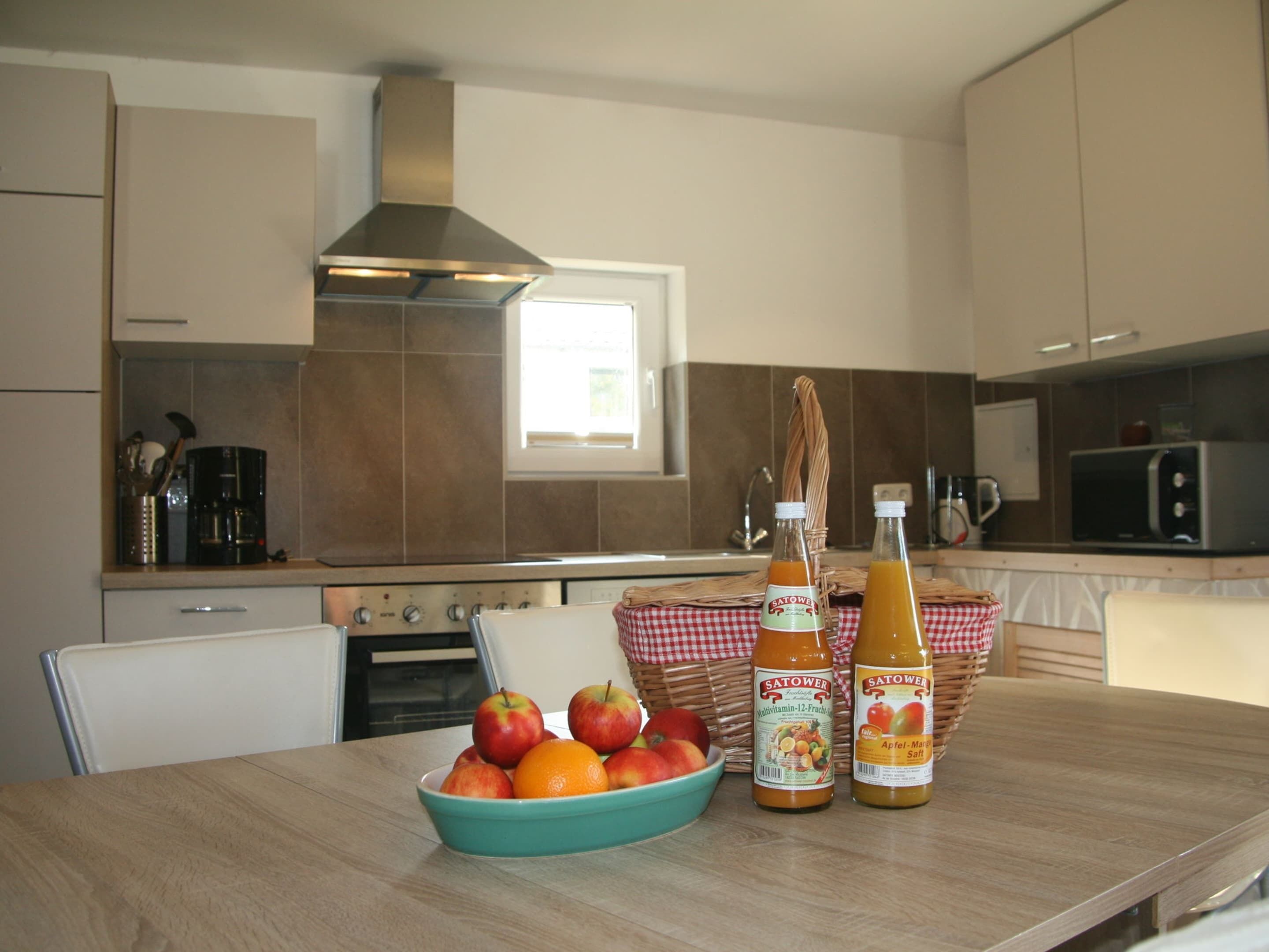 A kitchen with a wooden table, a bowl of fruit, and two bottles of juice.