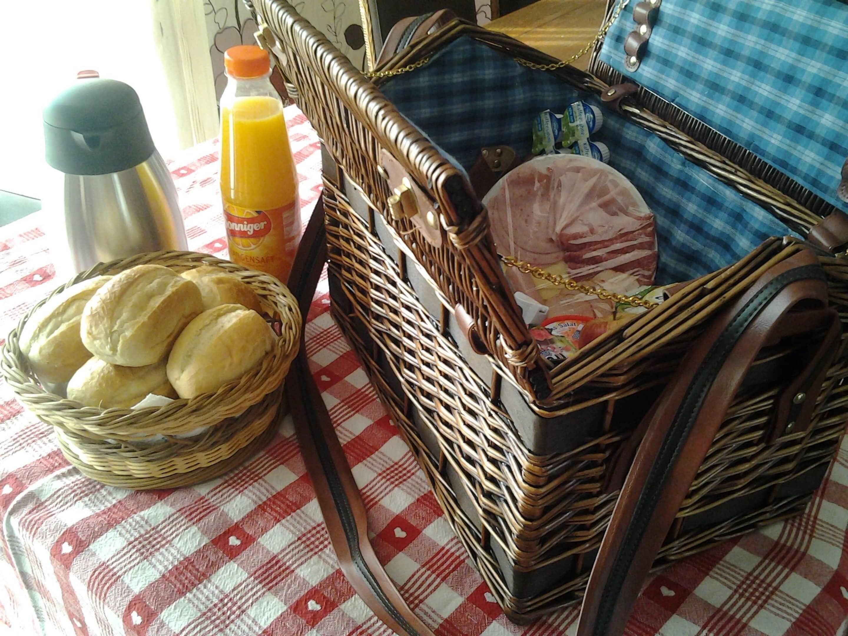 Una cesta de mimbre con pan, un termo y una botella de jugo de naranja sobre un mantel a cuadros.