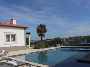 A pool area with lounge chairs and a view of a hill with houses. - Villa in Portugal With Private Pool & Wellness (Caldas da Rainha)
