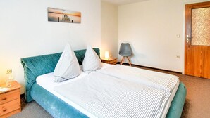 A neatly made bed with striped bedding and a teal headboard, a bedside table with a lamp, a chair, and a door with a textured panel. - Apartment in Klutz Near Baltic Sea Beach (Klütz)