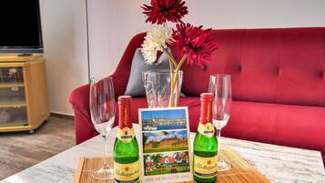 A table with two bottles of Rottkappfen beer, two wine glasses, a vase with red and white flowers, and a postcard of a scenic view.