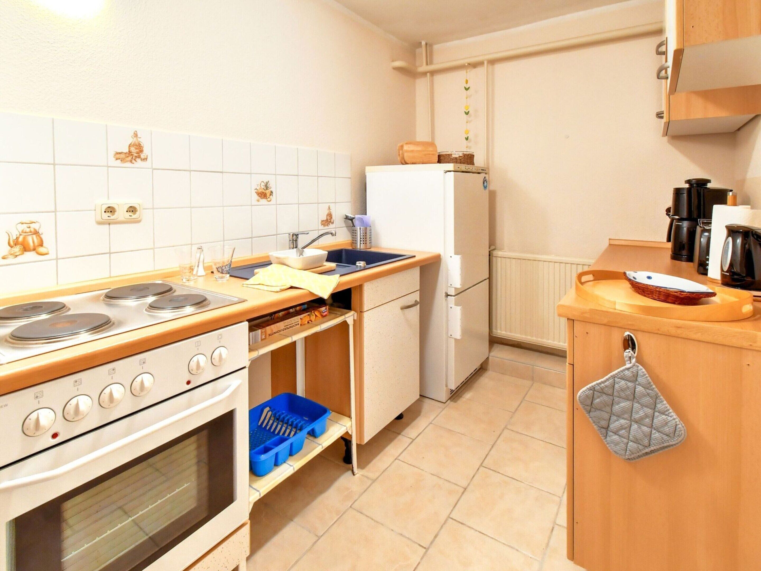 Een kleine keuken met witte kastjes, een fornuis, een spoelbak en een koelkast.
