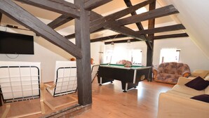 A cozy loft with exposed wooden beams, a pool table, a sofa, and a television. - Relaxation Holiday Home (Jiretin pod Jedlovou)