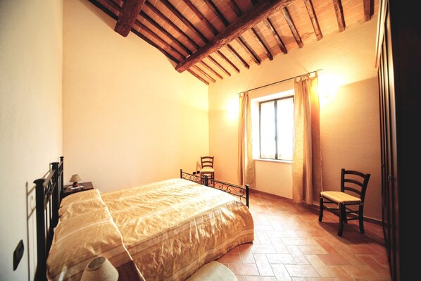 A bedroom with a bed, a chair, a window with curtains, and a wooden ceiling.