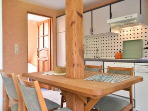 A dining area with a wooden table and chairs, a kitchen with a patterned backsplash, and a door leading to another room.