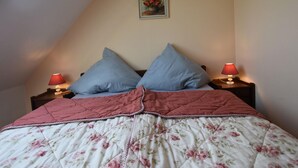 Ein Schlafzimmer mit schrägverdeckter Decke, einer blumigen Tagesdecke, zwei Kissen und zwei Nachttischlampen.