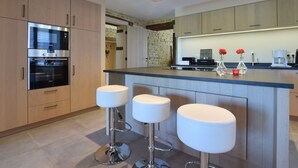 Una cuina moderna amb electrodomèstics integrats, una illa central amb tamborets i una paret d'accent de pedra.