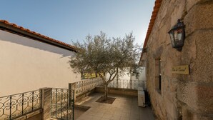 A courtyard with a tiled floor, a tree, a stone wall, and a metal fence. - Vila Flor Pool Retreat (Vila Flor)