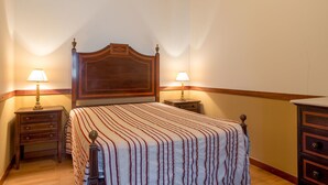 A bedroom with a wooden headboard, two bedside tables with lamps, a striped bedspread, and a wooden dresser. - Vila Flor Pool Retreat (Vila Flor)